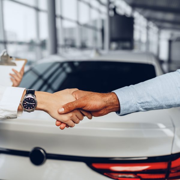 Woman car seller and man car buyer handshaking in car salon building